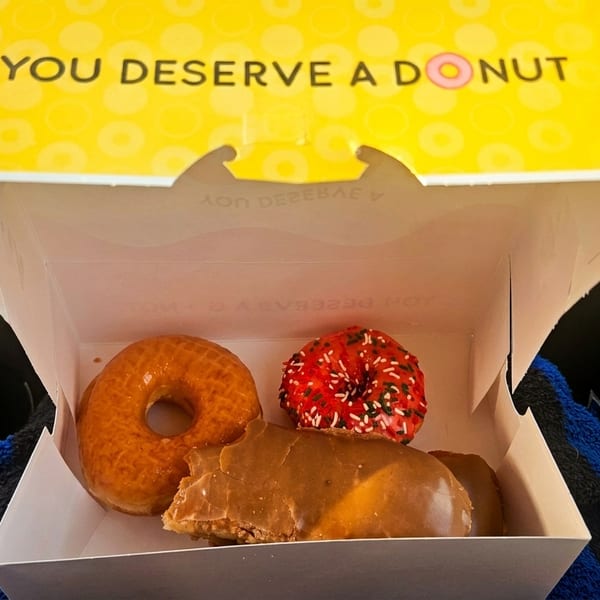 A Krispy Kreme box with "YOU DESERVE A DONUT" on the lid, containing three assorted donuts.