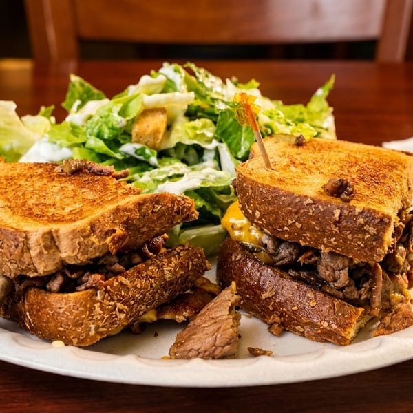 Grilled cheese sandwich with steak and cheese, served with a side salad on a white plate.