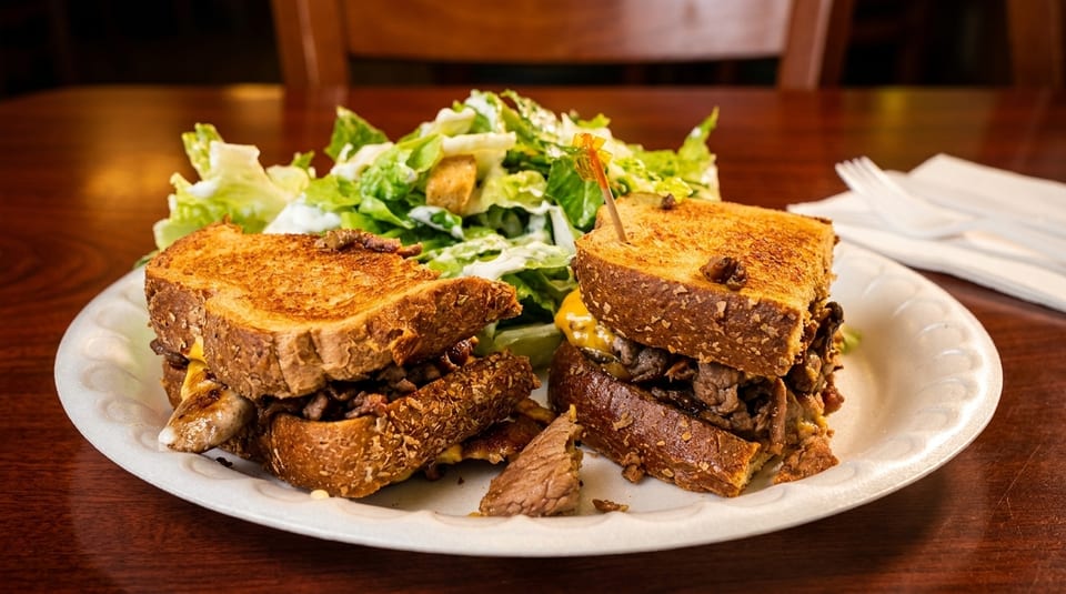 Grilled cheese sandwich with steak and cheese, served with a side salad on a white plate.